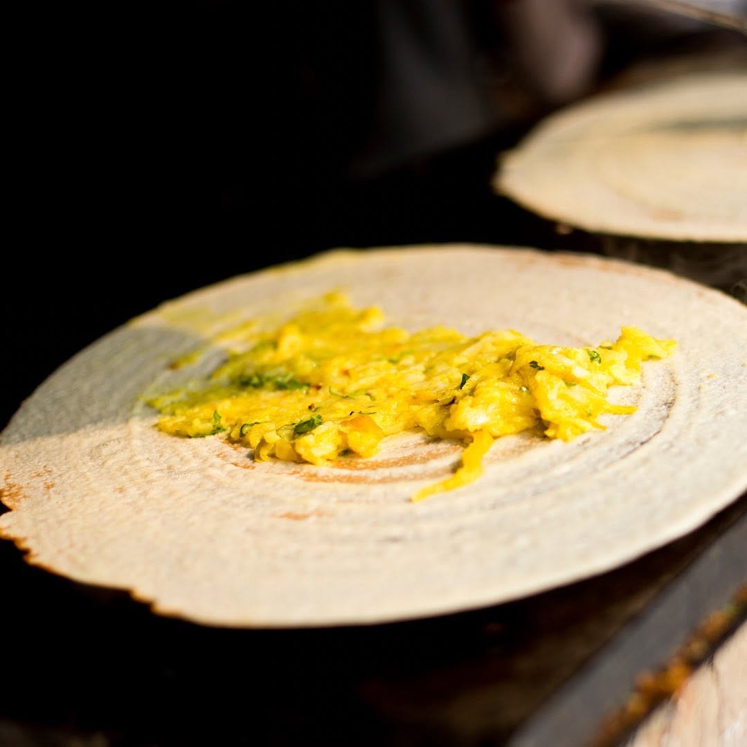 Dosa cooking on the tawa with egg spread across it
